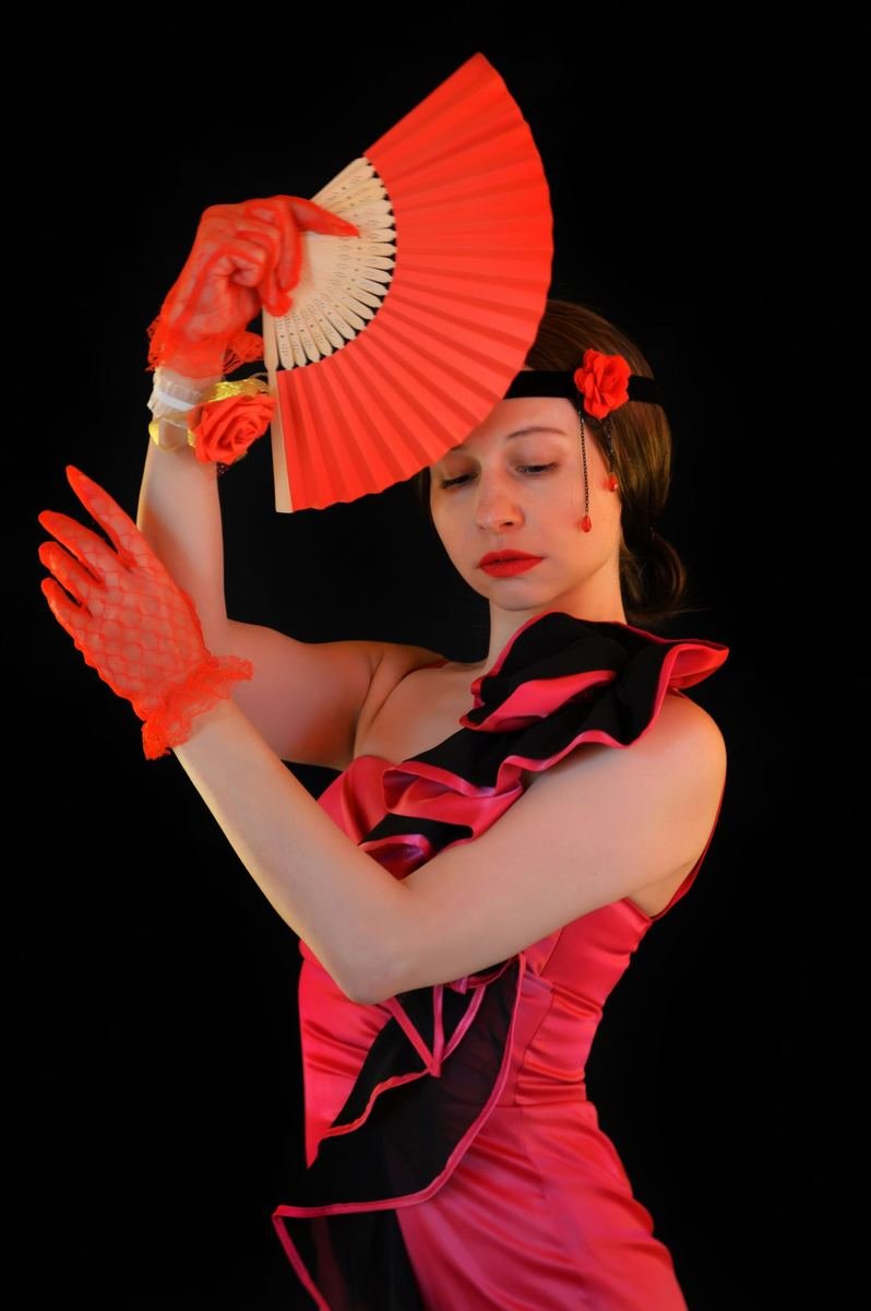Bailaora con traje de flamenco rojo y abanico sobre fondo negro